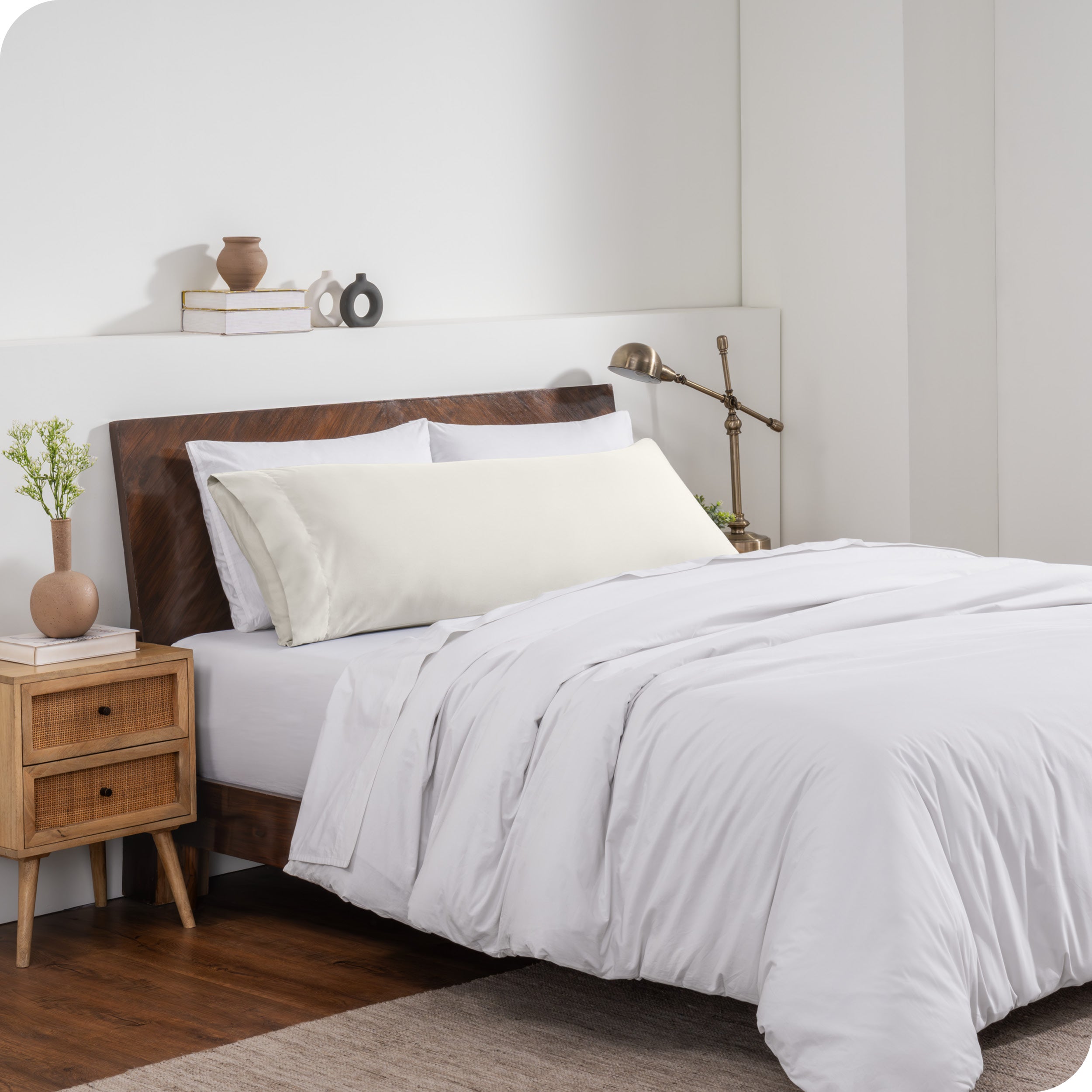 A body pillow cover on a pillow on a bed made with all white bedding