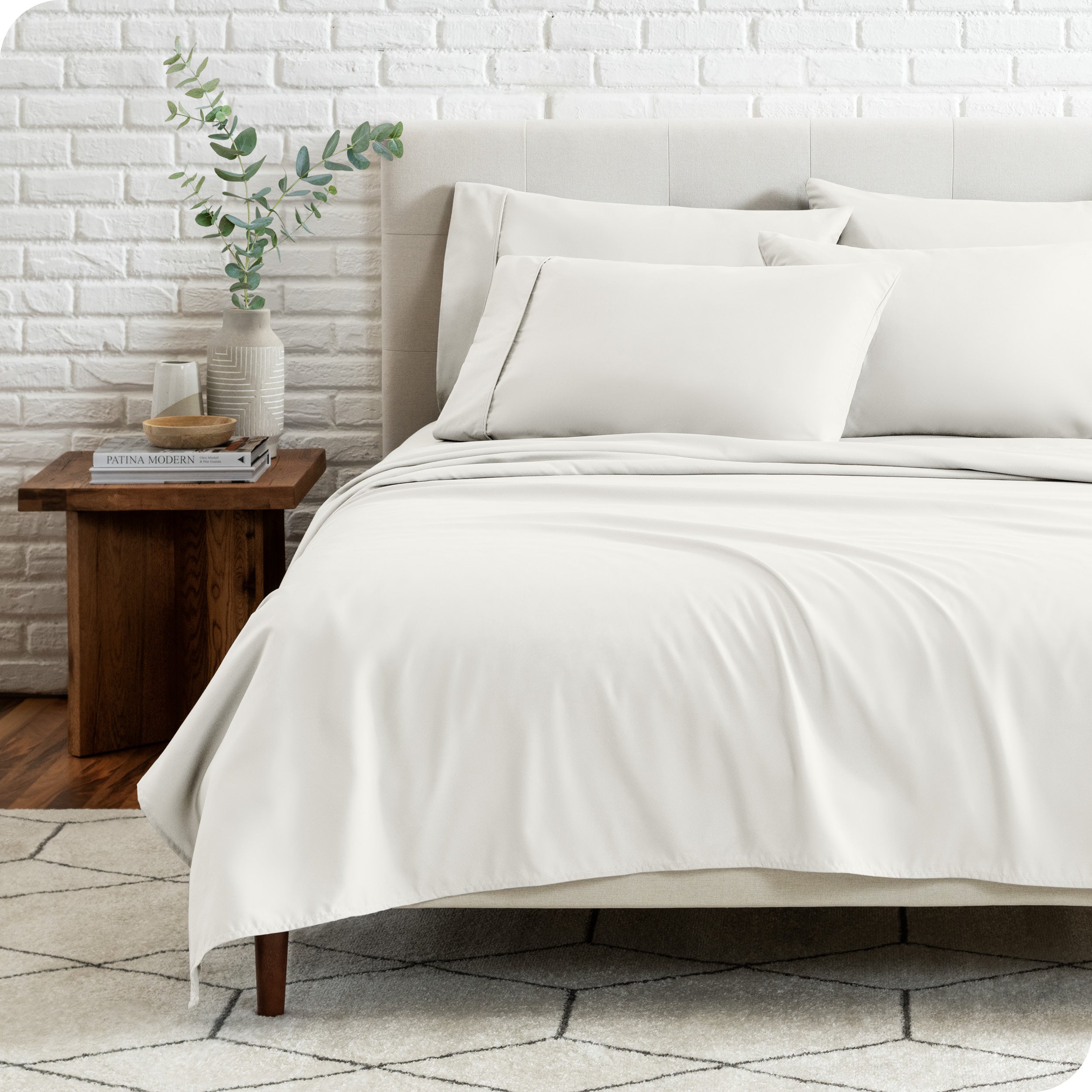 End view of a modern bed with the microfiber sheets on the bed with four pillows.