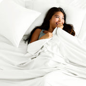 A smiling woman on a bed with a microfiber sheet over her
