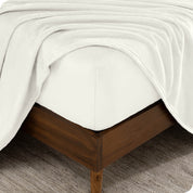 A corner of a mattress with a fitted sheet and a flat sheet on it.