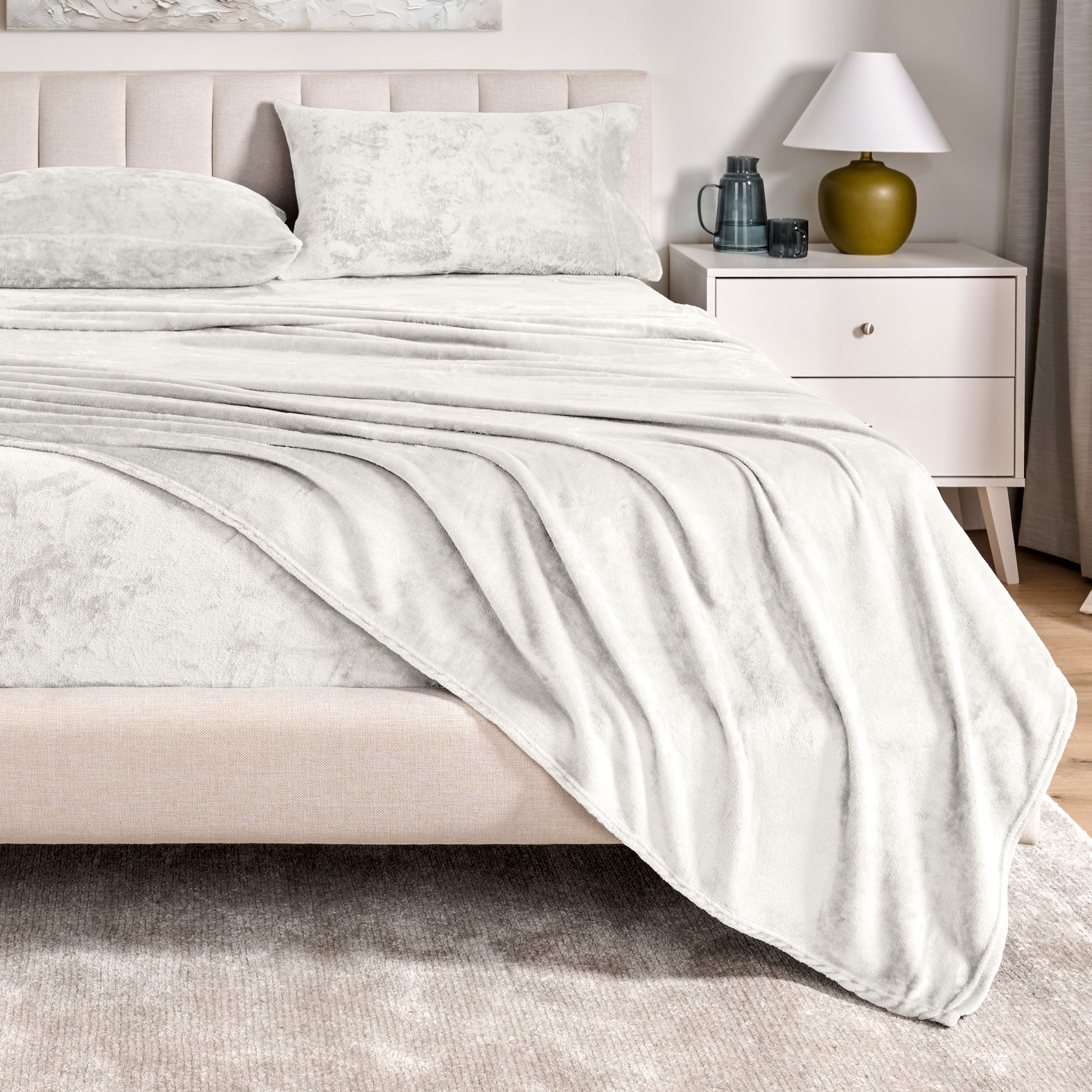 Microplush sheets on a bed in a bedroom setting with a nightstand and lamp.