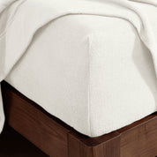Corner of the bed with a fitted sheet on the mattress and a flat sheet draped over the side and end