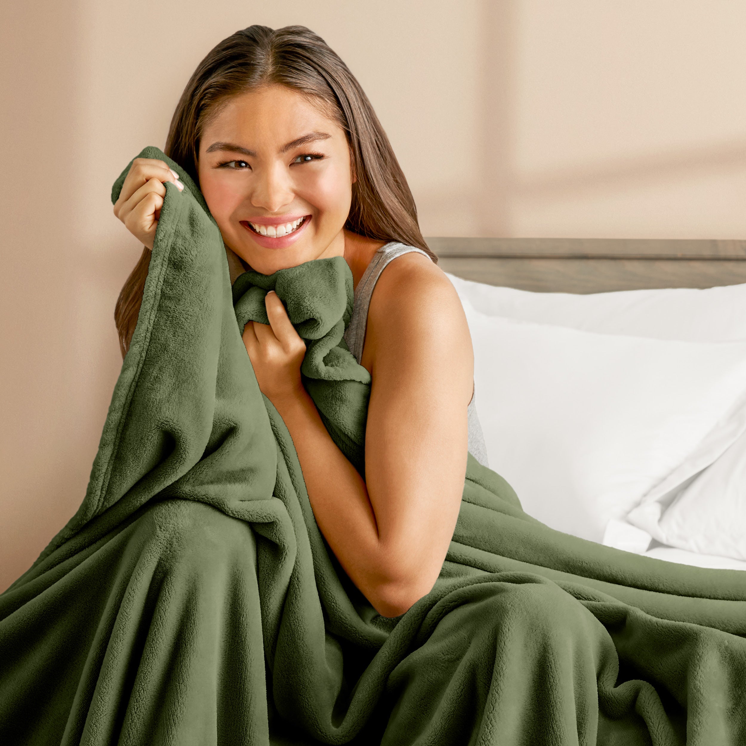 A woman sitting on a bed wrapped in a microplush blanket