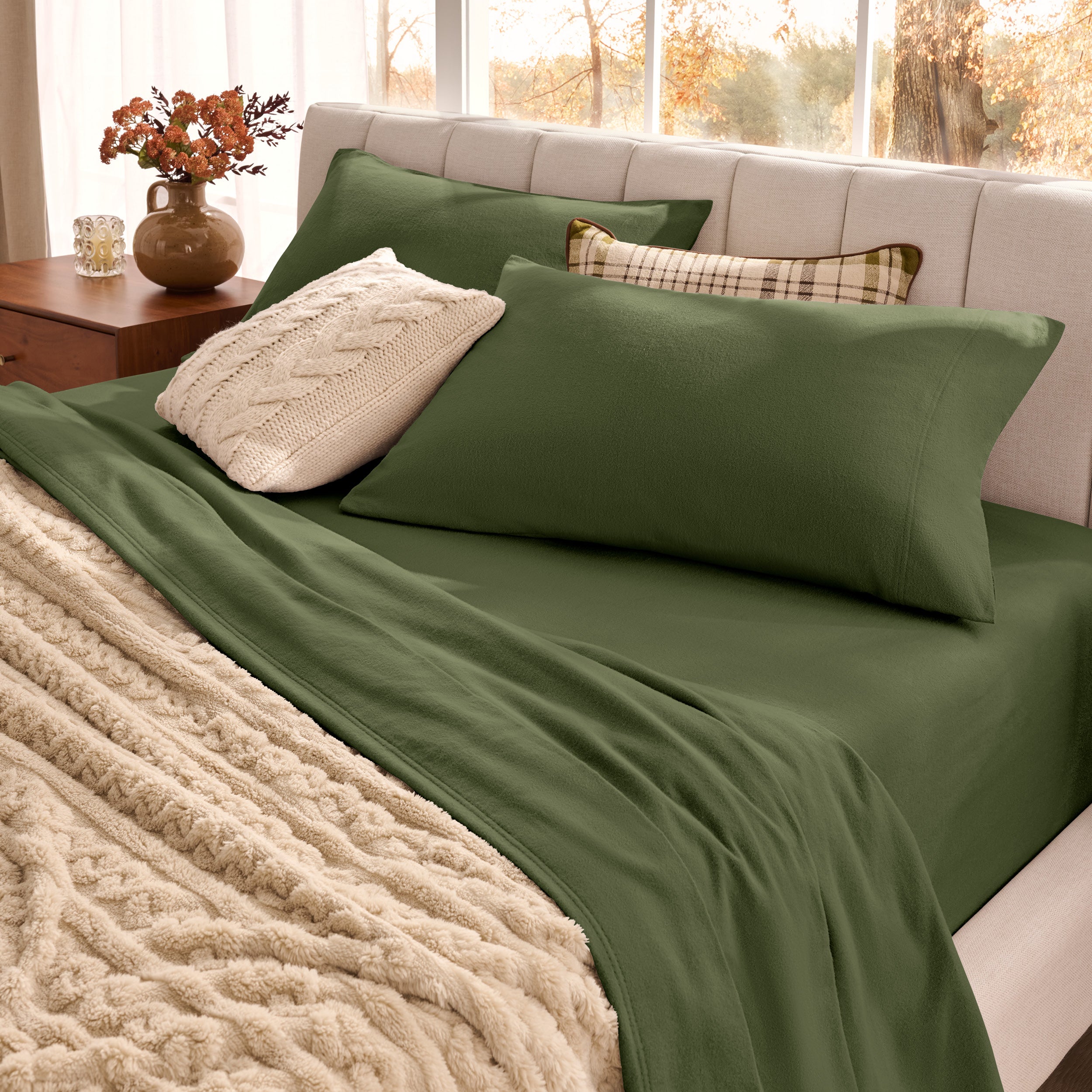 Neatly made bed with pillows and a beige blanket in a bright room.