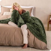 A woman sitting on the end of a bed with a shaggy blanket wrapped around her
