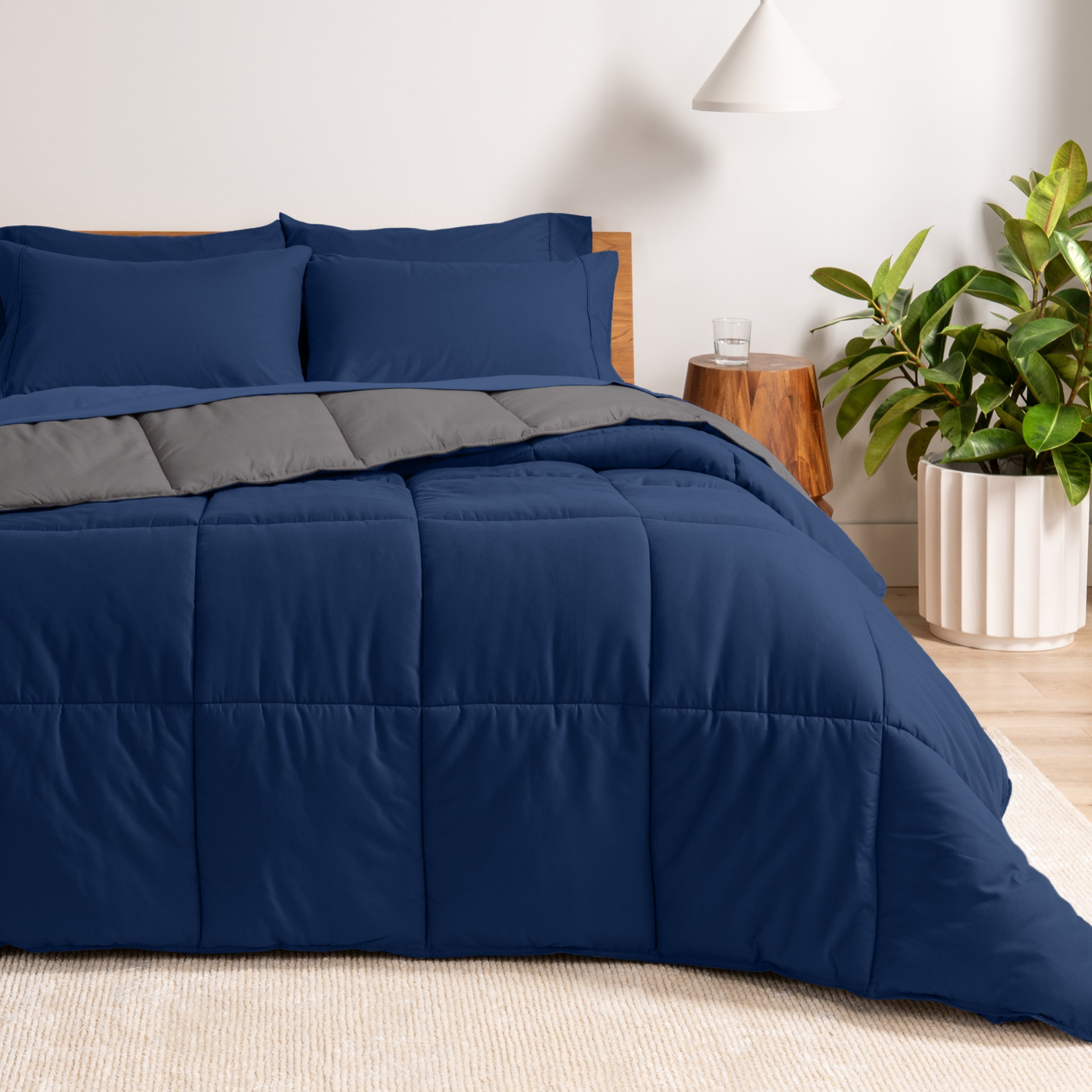 A wooden bed frame with a reversible comforter and sheet set on the mattress in a bright warm room.