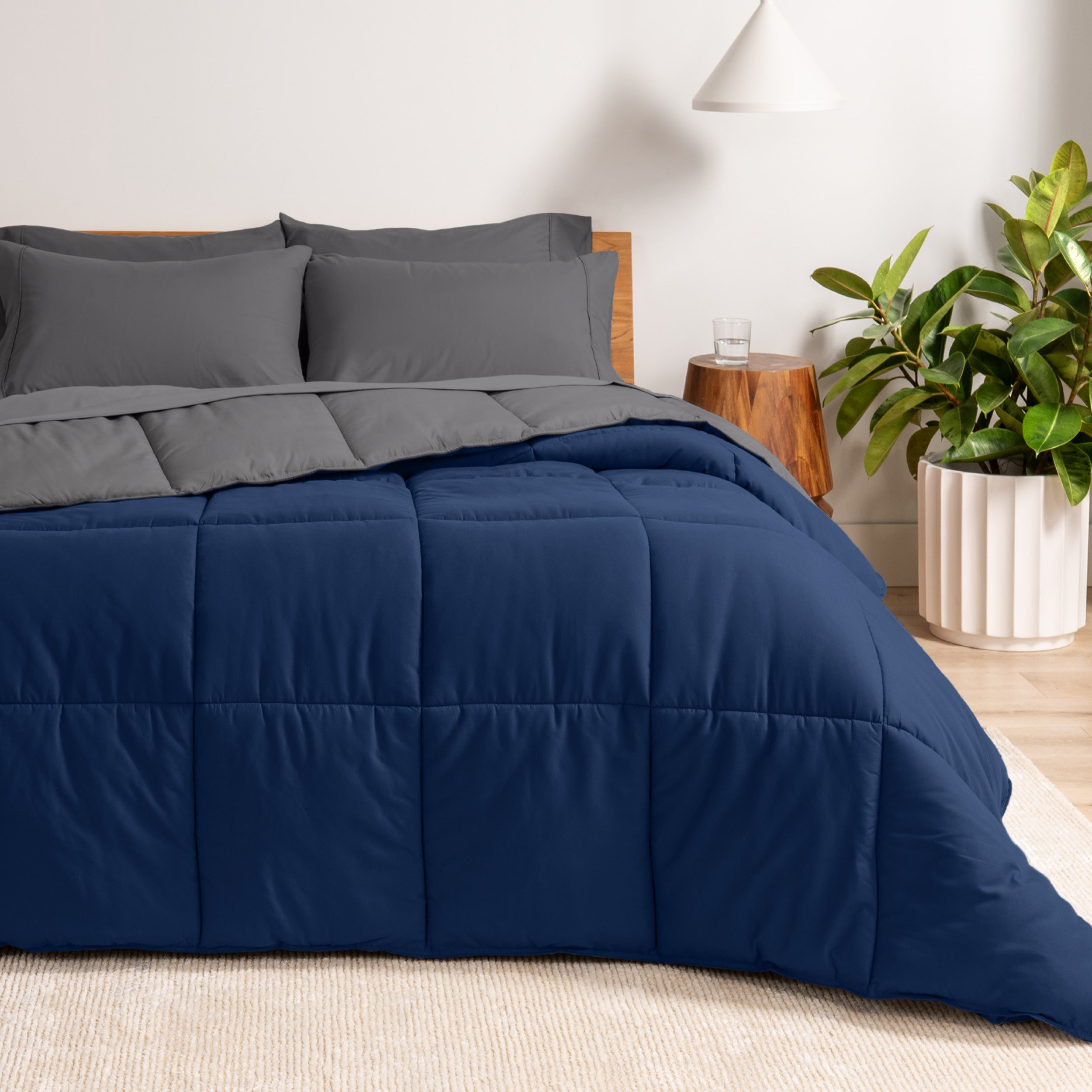 A wooden bed frame with a reversible comforter and sheet set on the mattress in a bright warm room.