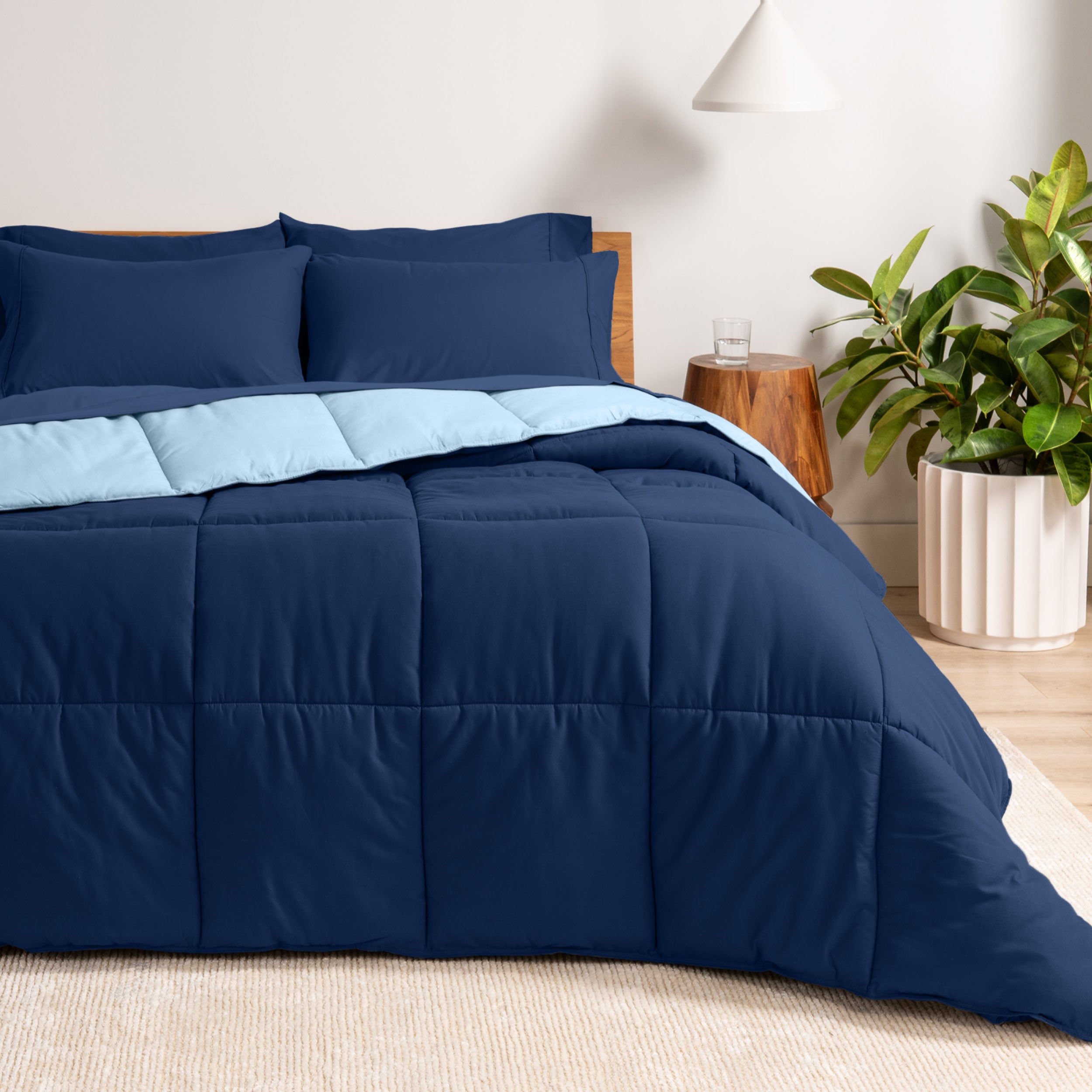 A wooden bed frame with a reversible comforter and sheet set on the mattress in a bright warm room.