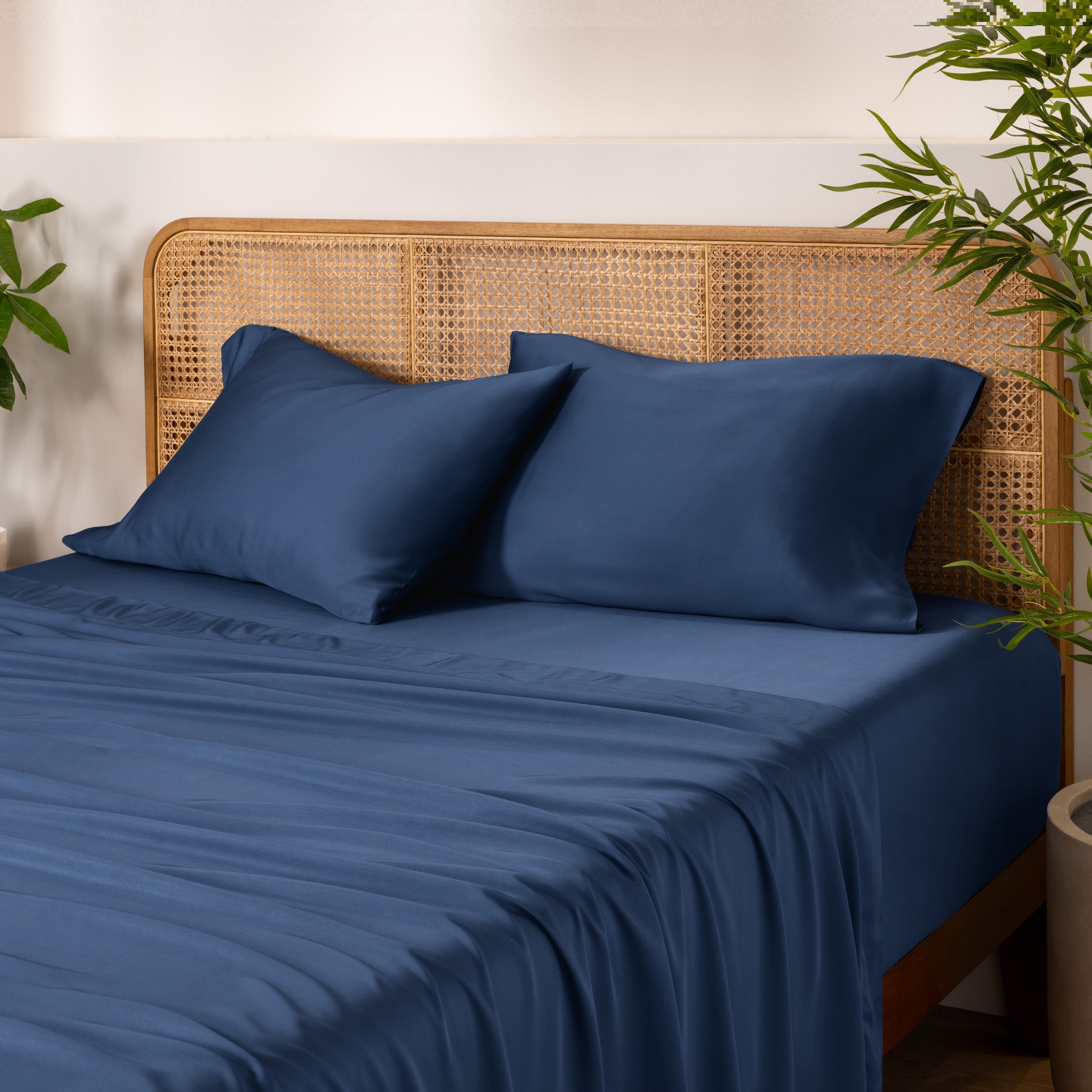 Bamboo bed sheets and pillowcases on a bed with a wicker headboard and plants in the background.
