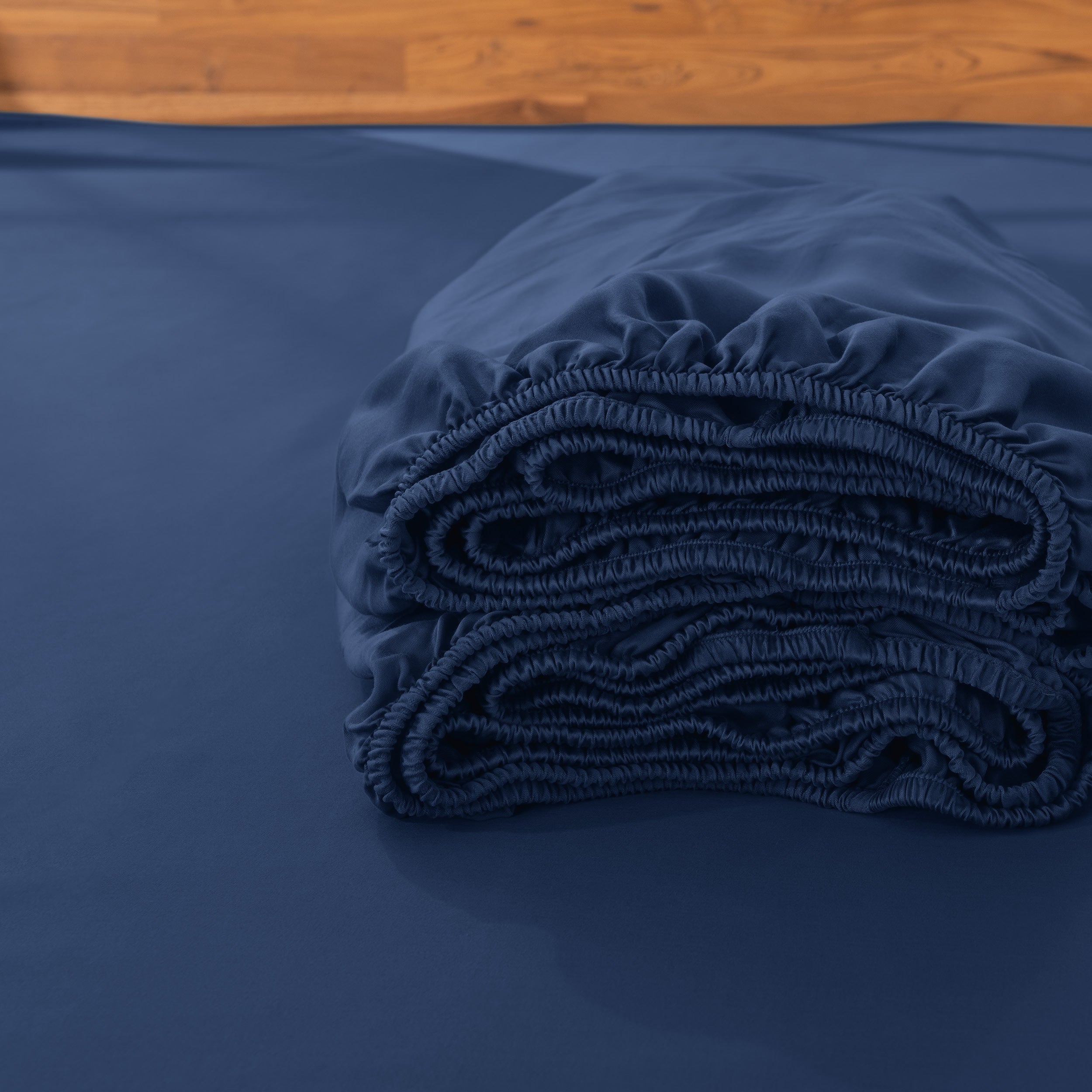 Folded fitted sheet on a bed with a wooden headboard.
