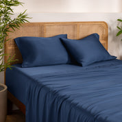 Bamboo bed sheets and pillowcases on a bed with a wicker headboard in a room with plants.