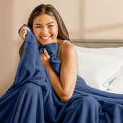 A woman sitting on a bed wrapped in a microplush blanket