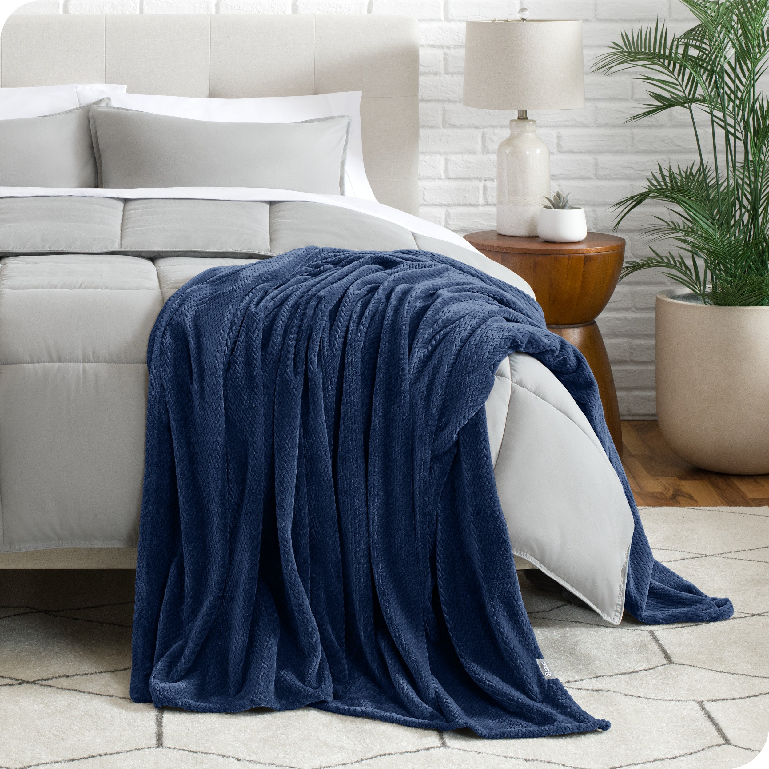 A textured microplush blanket is hanging over the corner of a bed