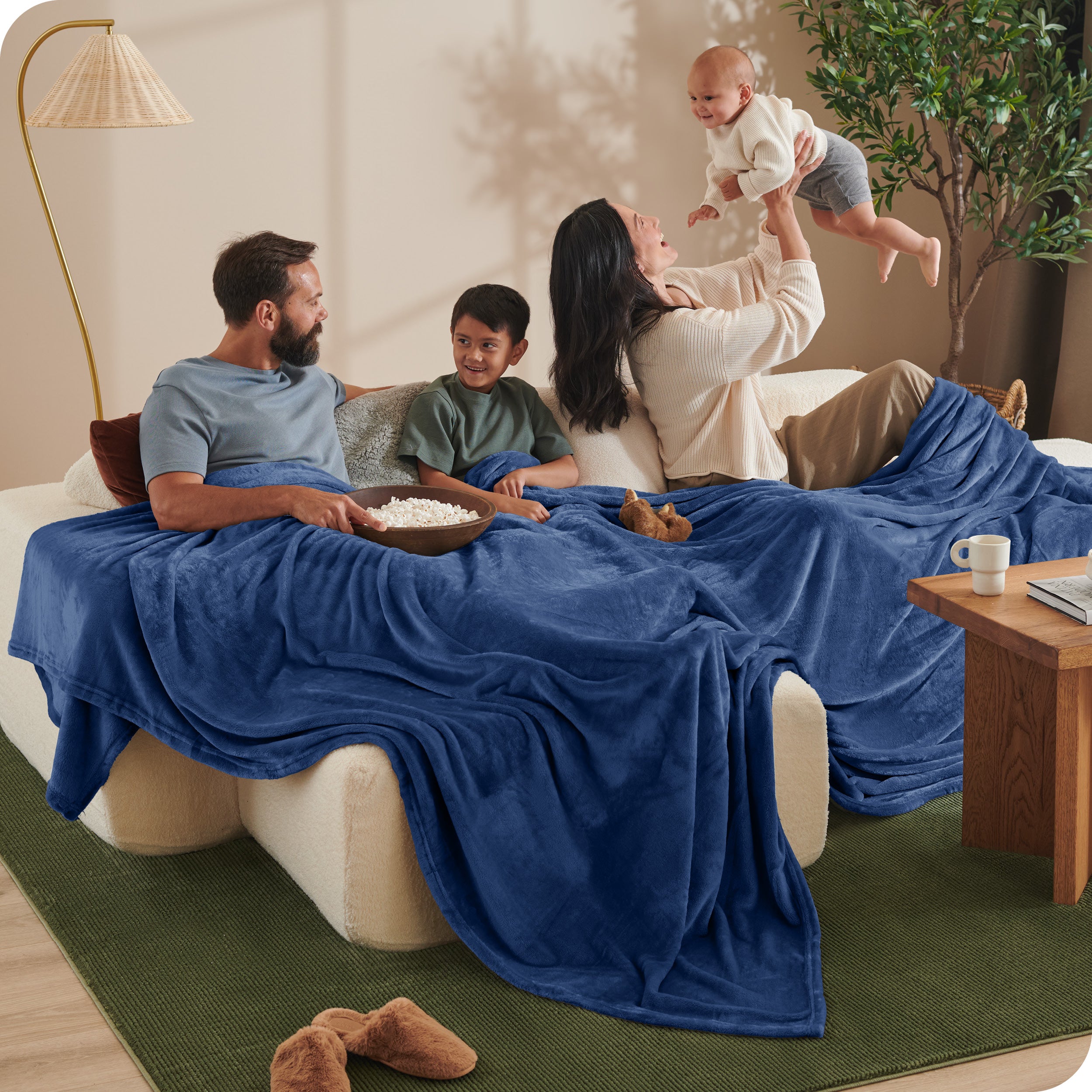 A family sitting on a couch with a giant microplush blanket covering them