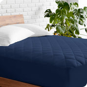 A modern bed with a wooden bed frame with a quilted mattress pad on.
