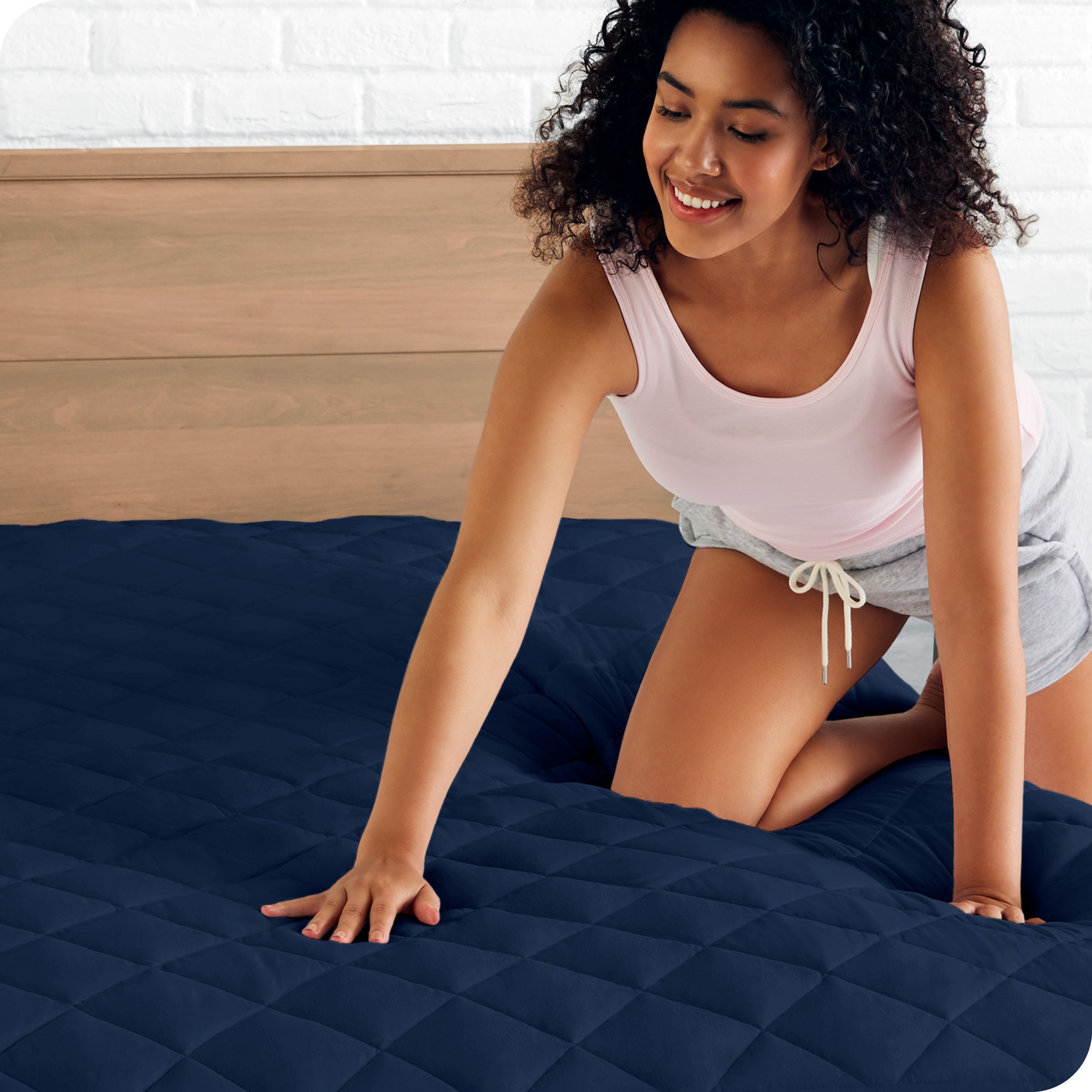 A woman is pushed her hand down on a quilted mattress pad on the bed