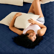 A women is laying on the bed with quilted mattress pad from above.