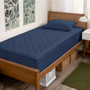 A bed with a wooden bed frame with a quilted mattress pad on.
