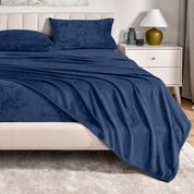 Microplush sheets on a bed in a bedroom setting with a nightstand and lamp.