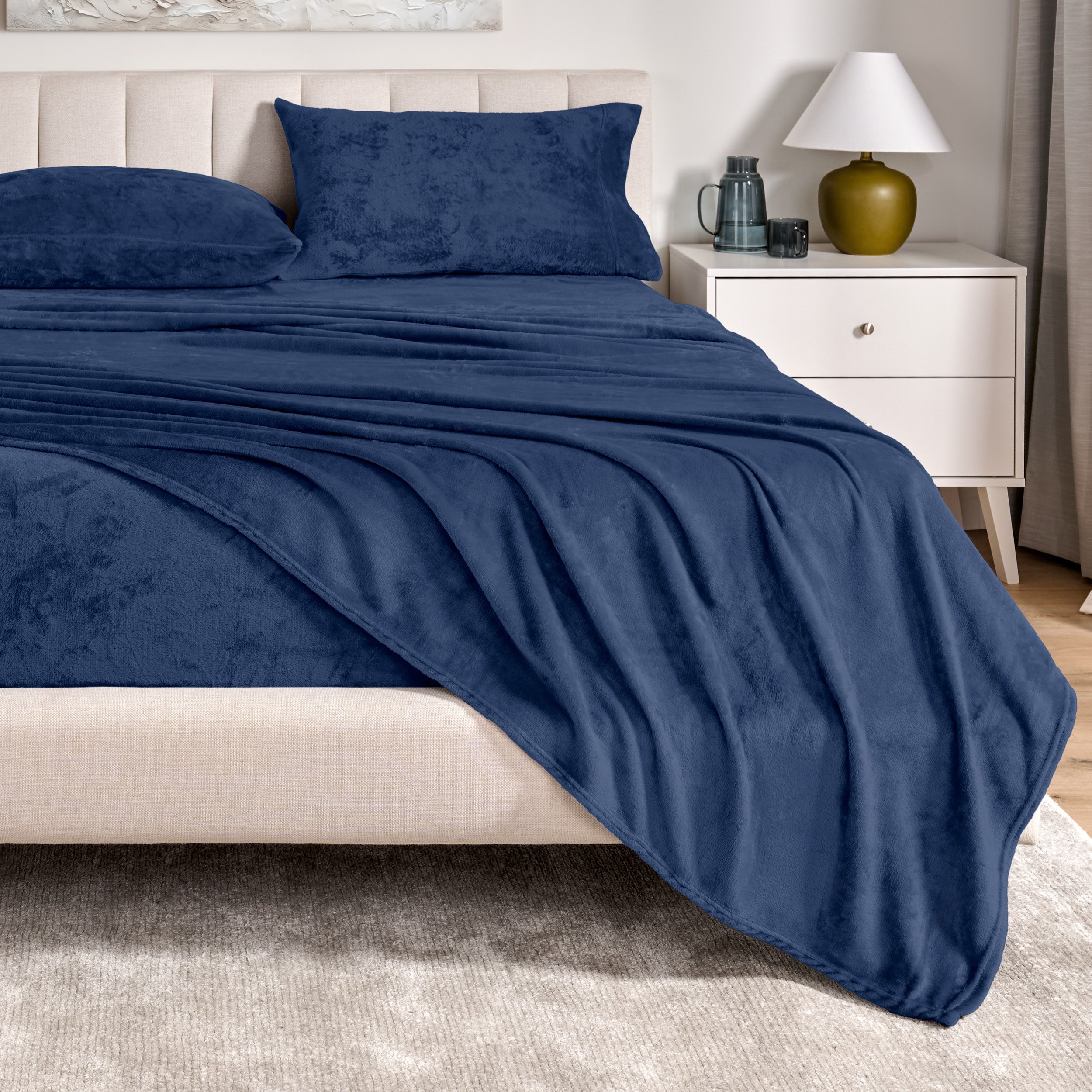 Microplush sheets on a bed in a bedroom setting with a nightstand and lamp.