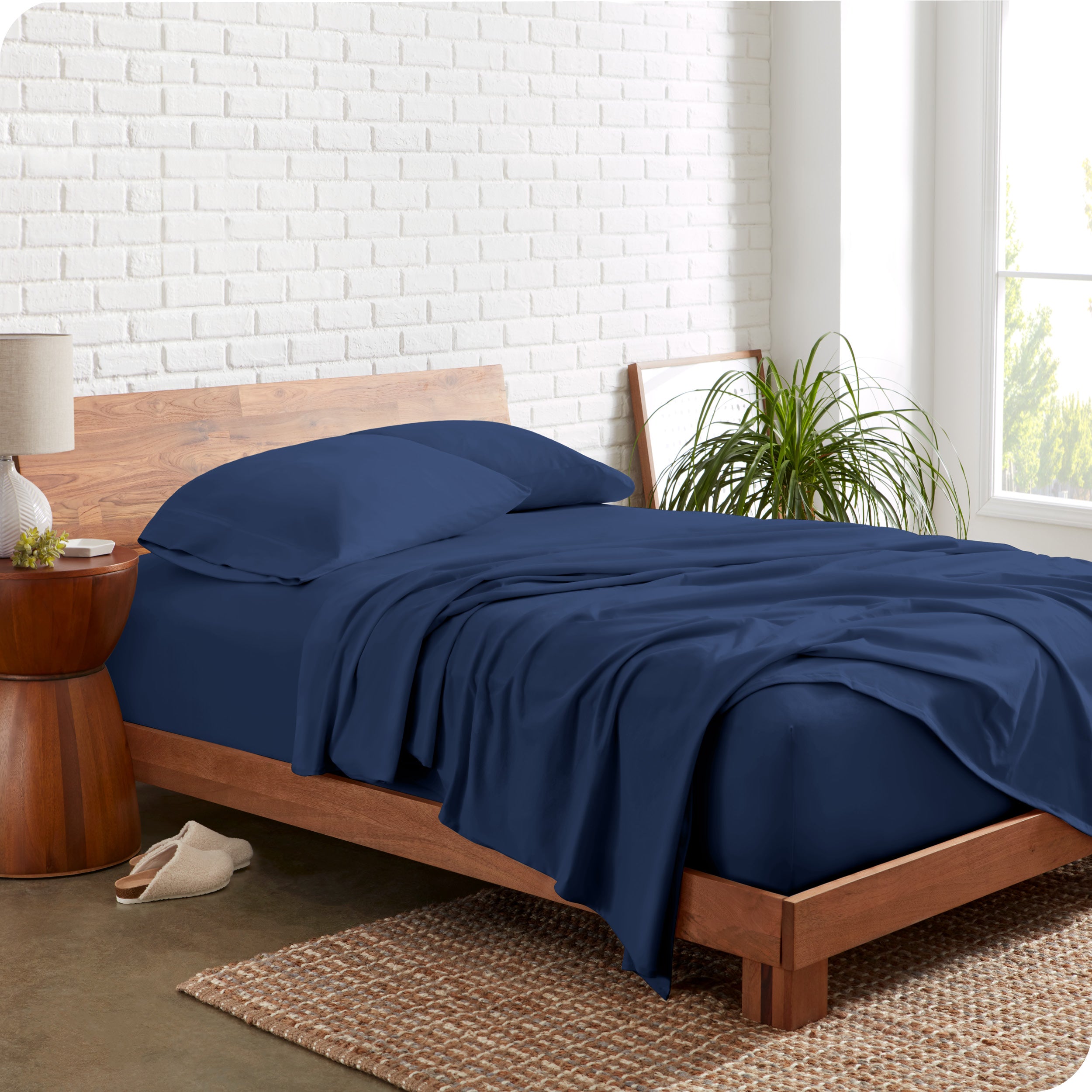 Organic jersey sheets on a bed with a brick wall behind the headboard