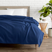 A polar fleece blanket on a bed next to a table and a large plant