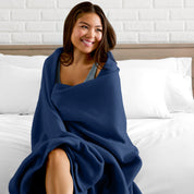 A woman sitting at the end of a bed with a fleece blanket wrapped around her shoulders