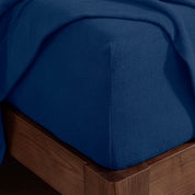 Corner of the bed with a fitted sheet on the mattress and a flat sheet draped over the side and end