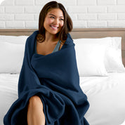 A woman sitting at the end of a bed with a fleece blanket wrapped around her shoulders