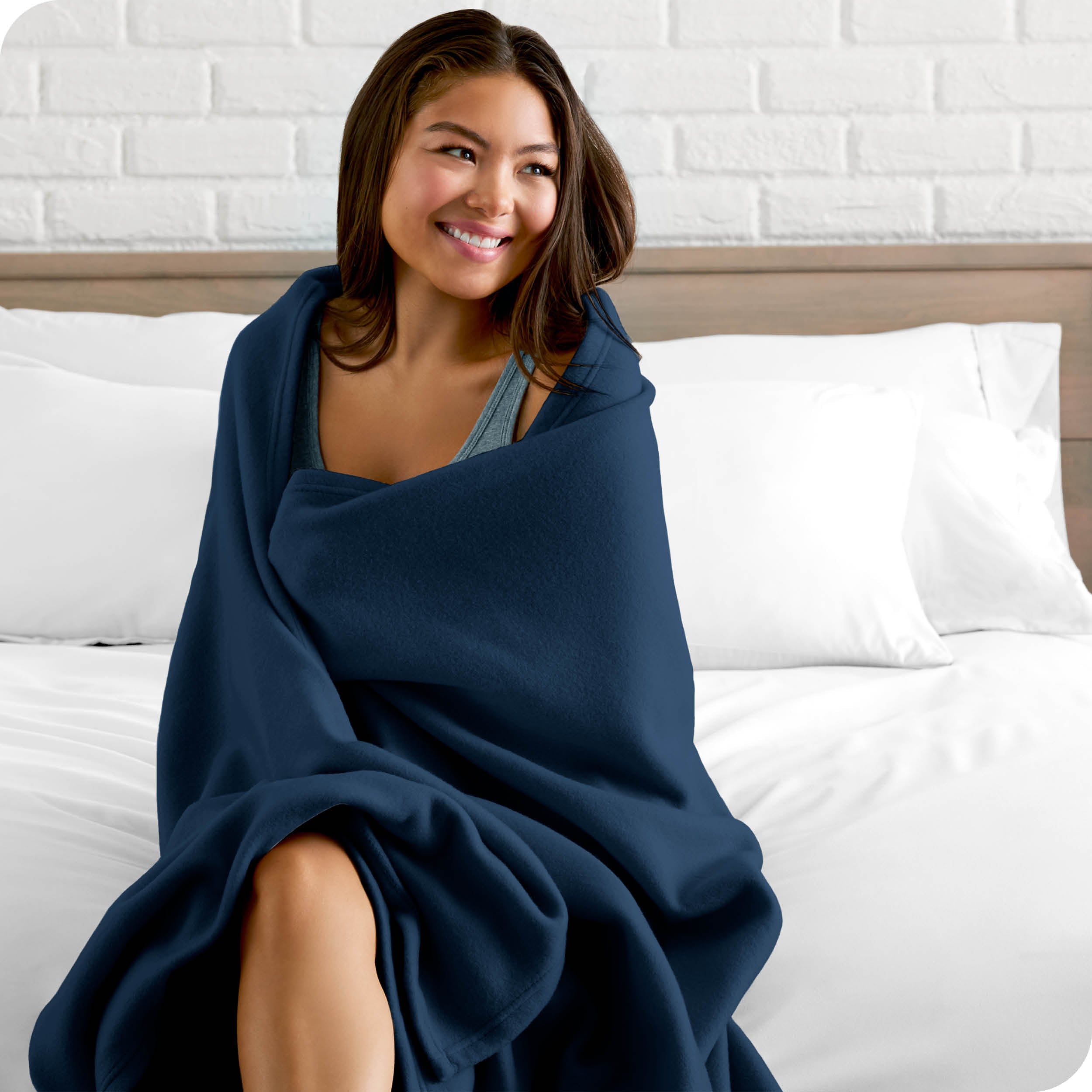 A woman sitting at the end of a bed with a fleece blanket wrapped around her shoulders