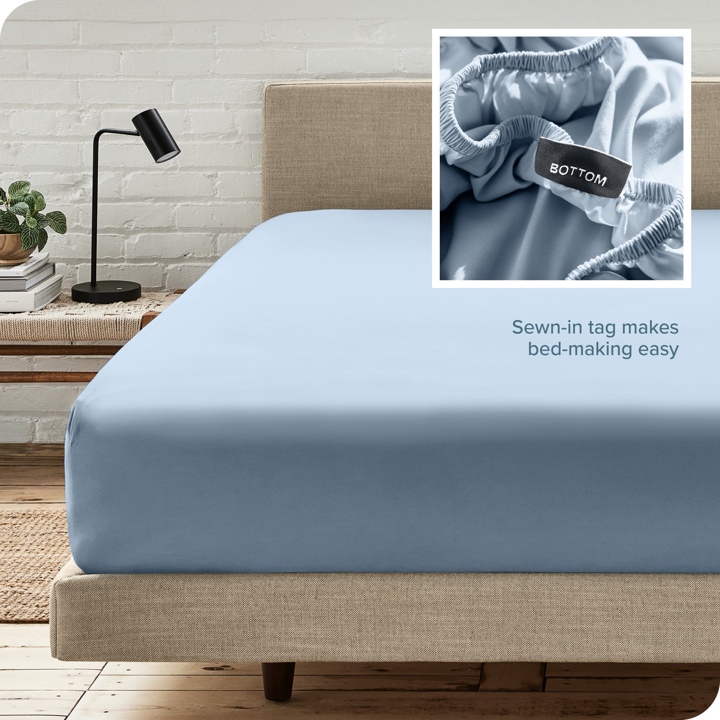 Closer end of the bed with a microfiber fitted sheet on the mattress, featuring a close-up of a sewn-in bottom tag in the upper left corner.