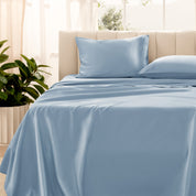 Organic sateen bedding on a bed with a beige headboard and plant in the corner.