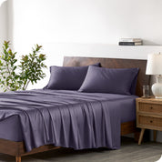Modern bedroom with a bed against a white wall with a nightstand next to the bed. The bed has bamboo sheets draped over it.