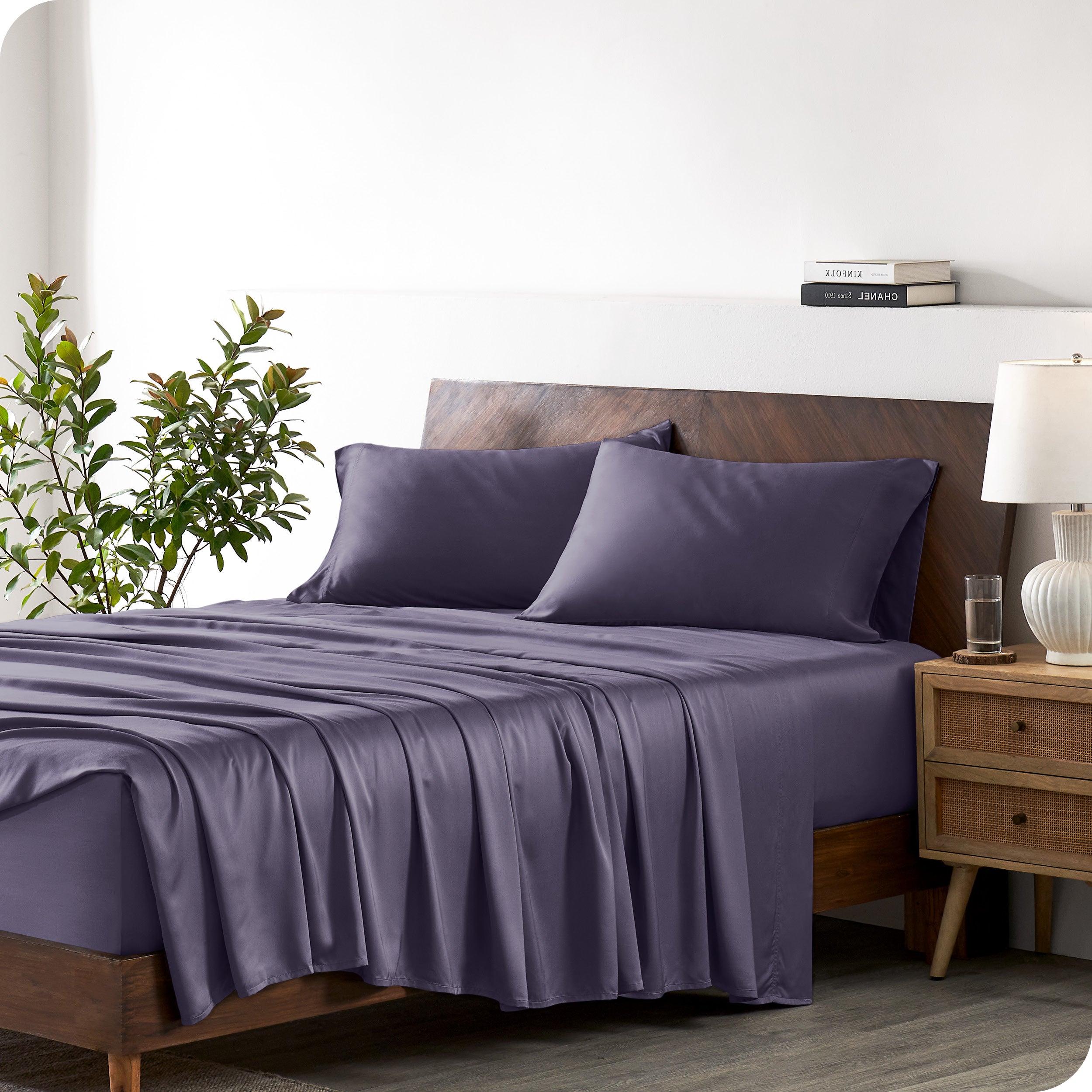 Modern bedroom with a bed against a white wall with a nightstand next to the bed. The bed has bamboo sheets draped over it.