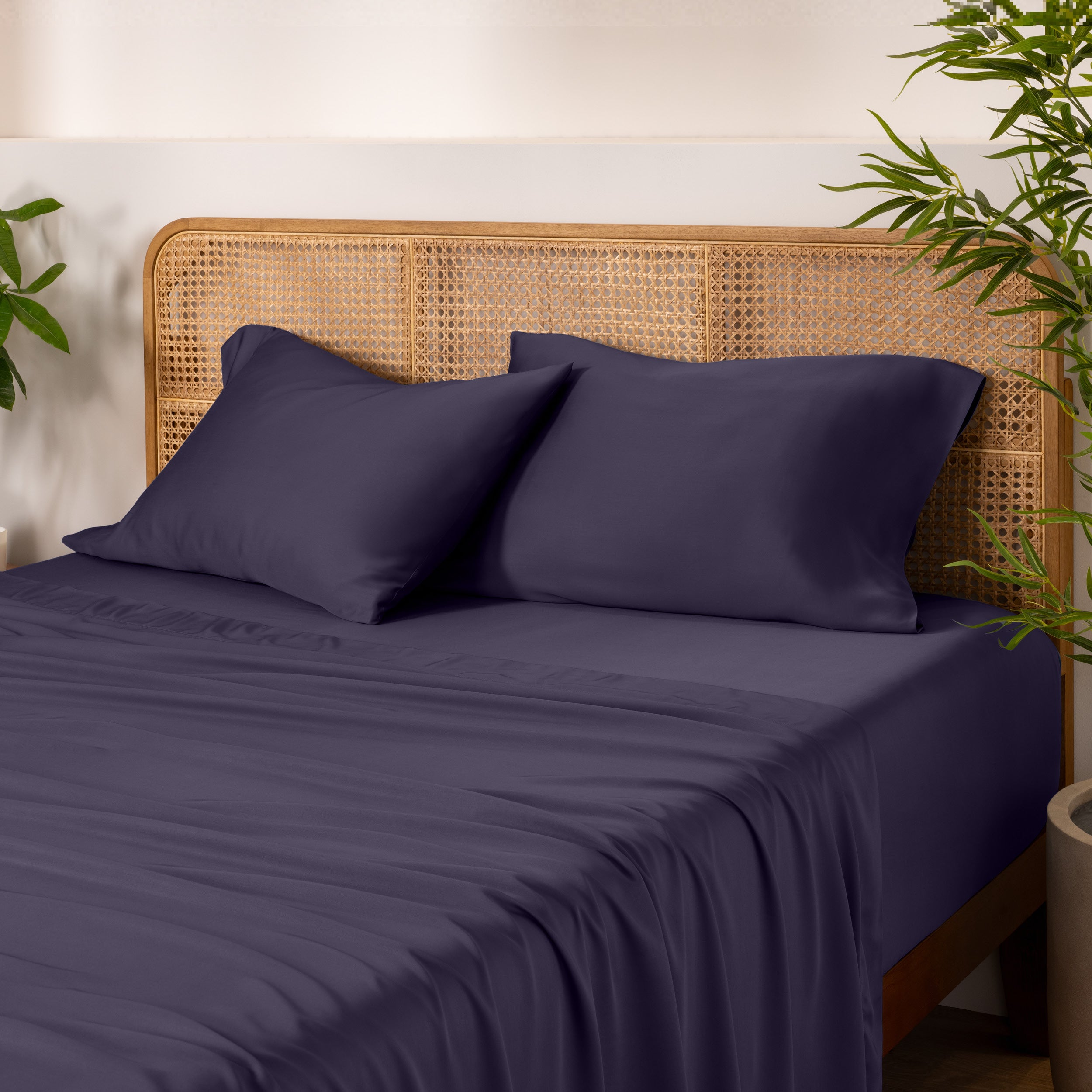 Bamboo bed sheets and pillowcases on a bed with a wicker headboard and plants in the background.