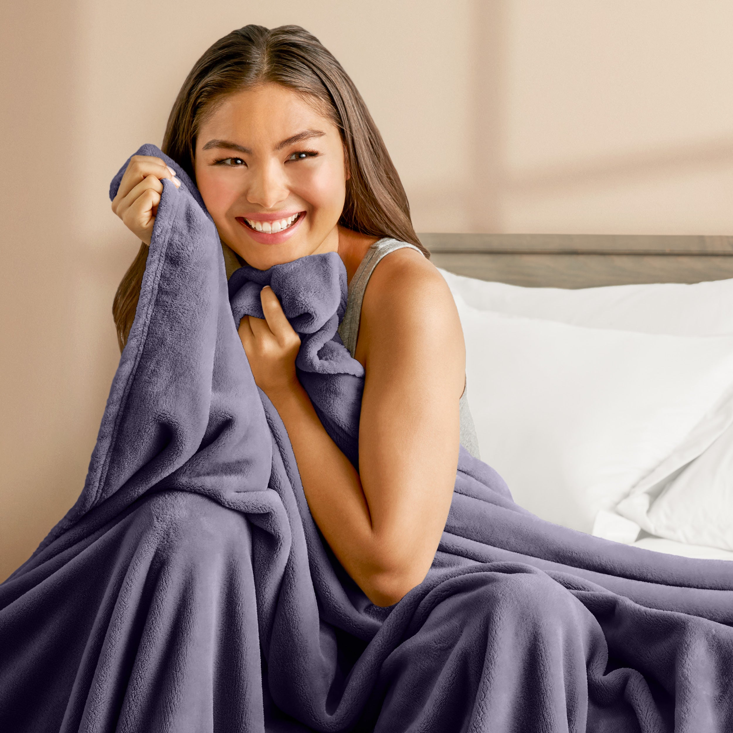 A woman sitting on a bed wrapped in a microplush blanket