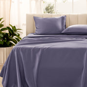 Organic sateen bedding on a bed with a beige headboard and plant in the corner.