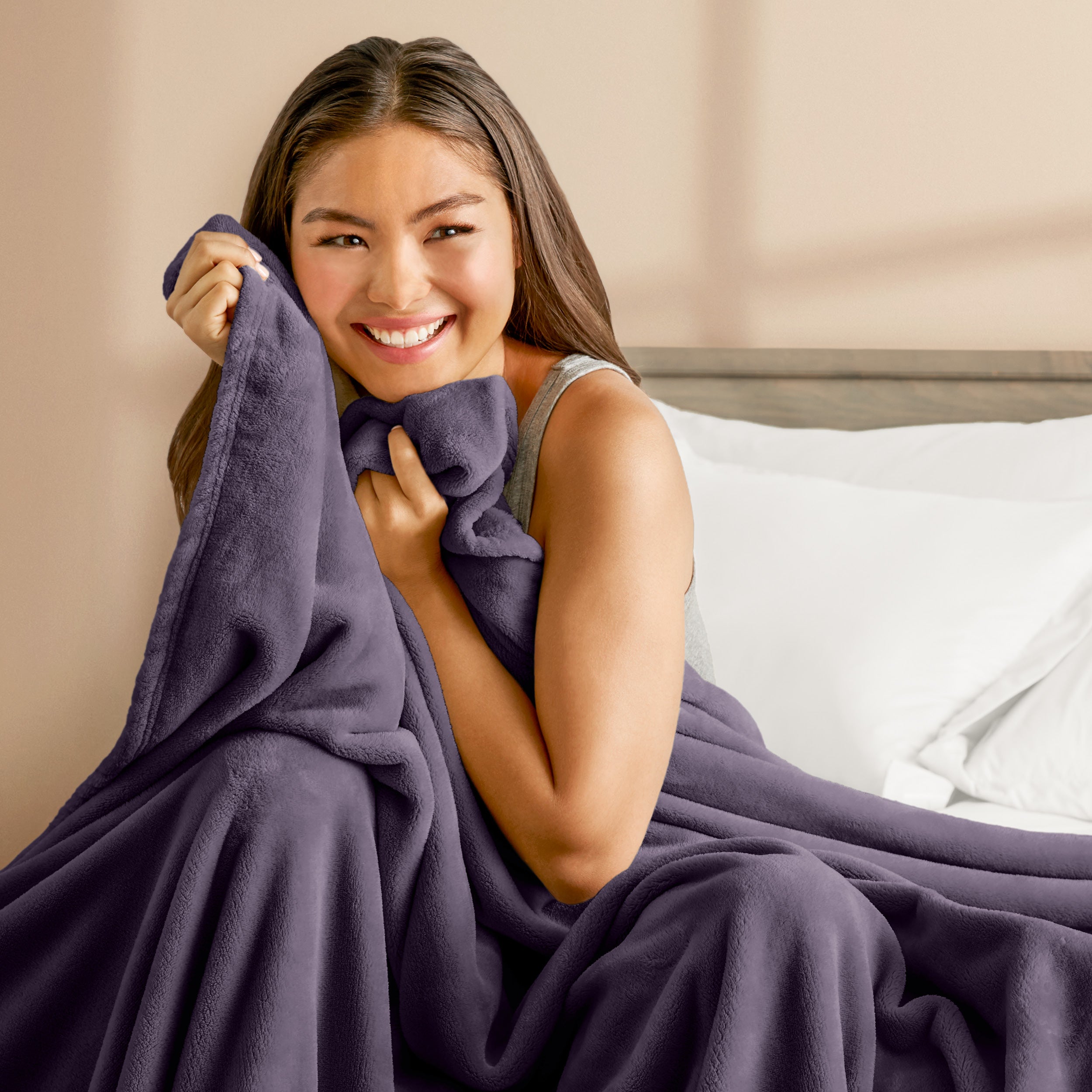A woman sitting on a bed wrapped in a microplush blanket