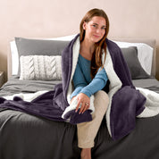 Woman cuddling with a sherpa blanket while sitting on the end of a bed