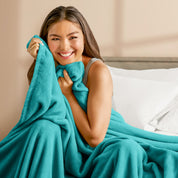 A woman sitting on a bed wrapped in a microplush blanket