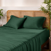 Bamboo bed sheets and pillowcases on a bed with a wicker headboard and plants in the background.