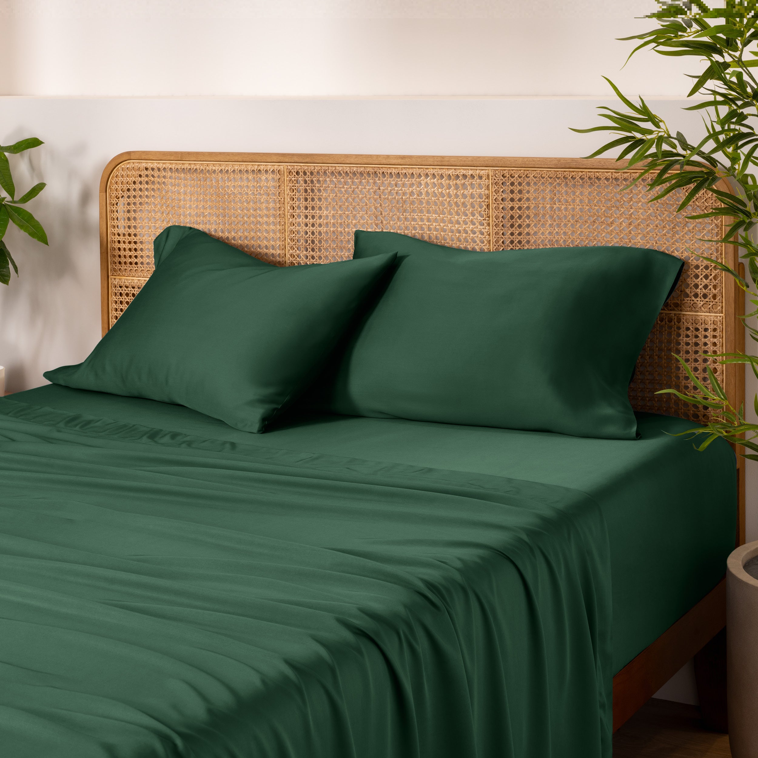 Bamboo bed sheets and pillowcases on a bed with a wicker headboard and plants in the background.