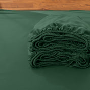 Folded fitted sheet on a bed with a wooden headboard.
