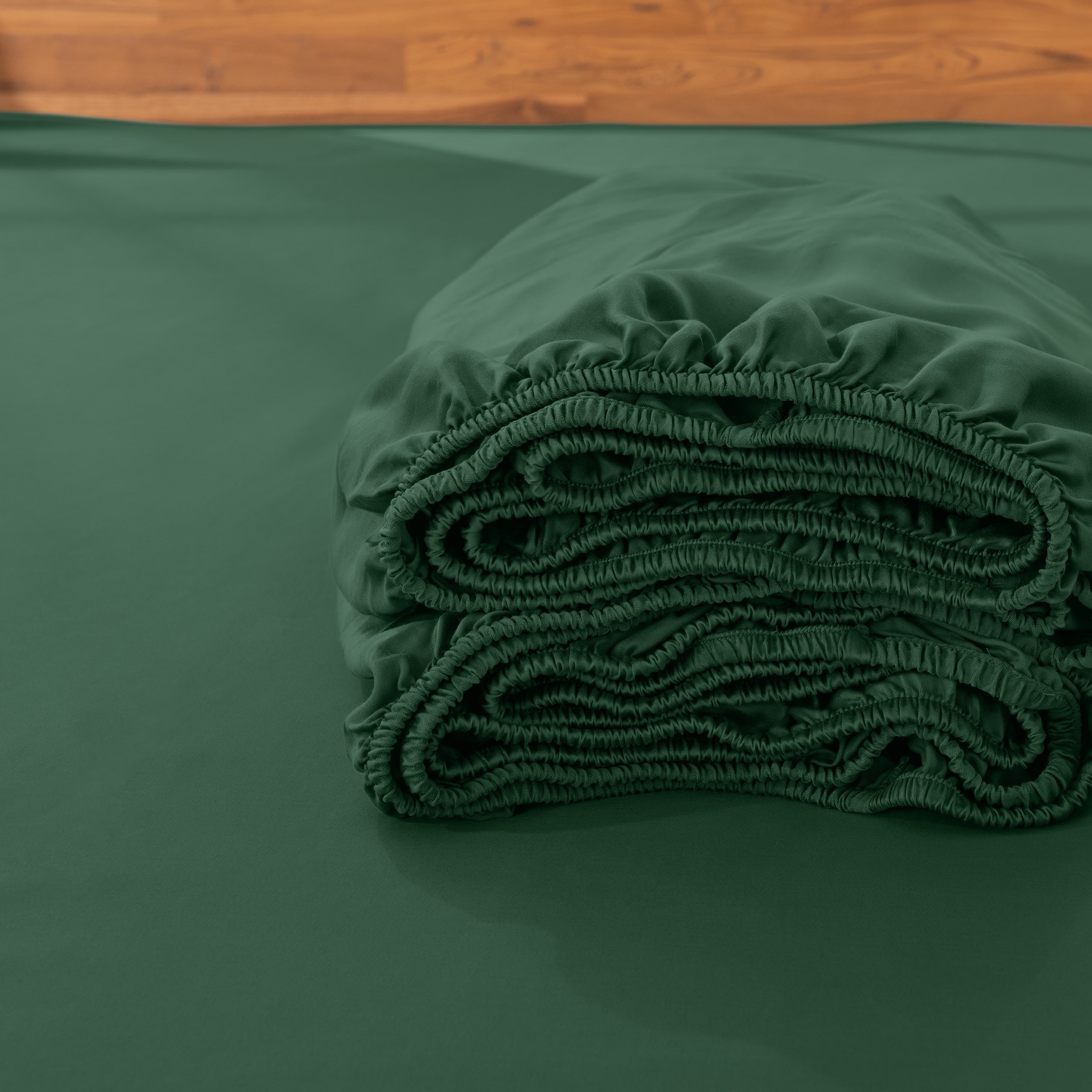 Folded fitted sheet on a bed with a wooden headboard.