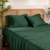 Bamboo bed sheets and pillowcases on a bed with a wicker headboard in a room with plants.