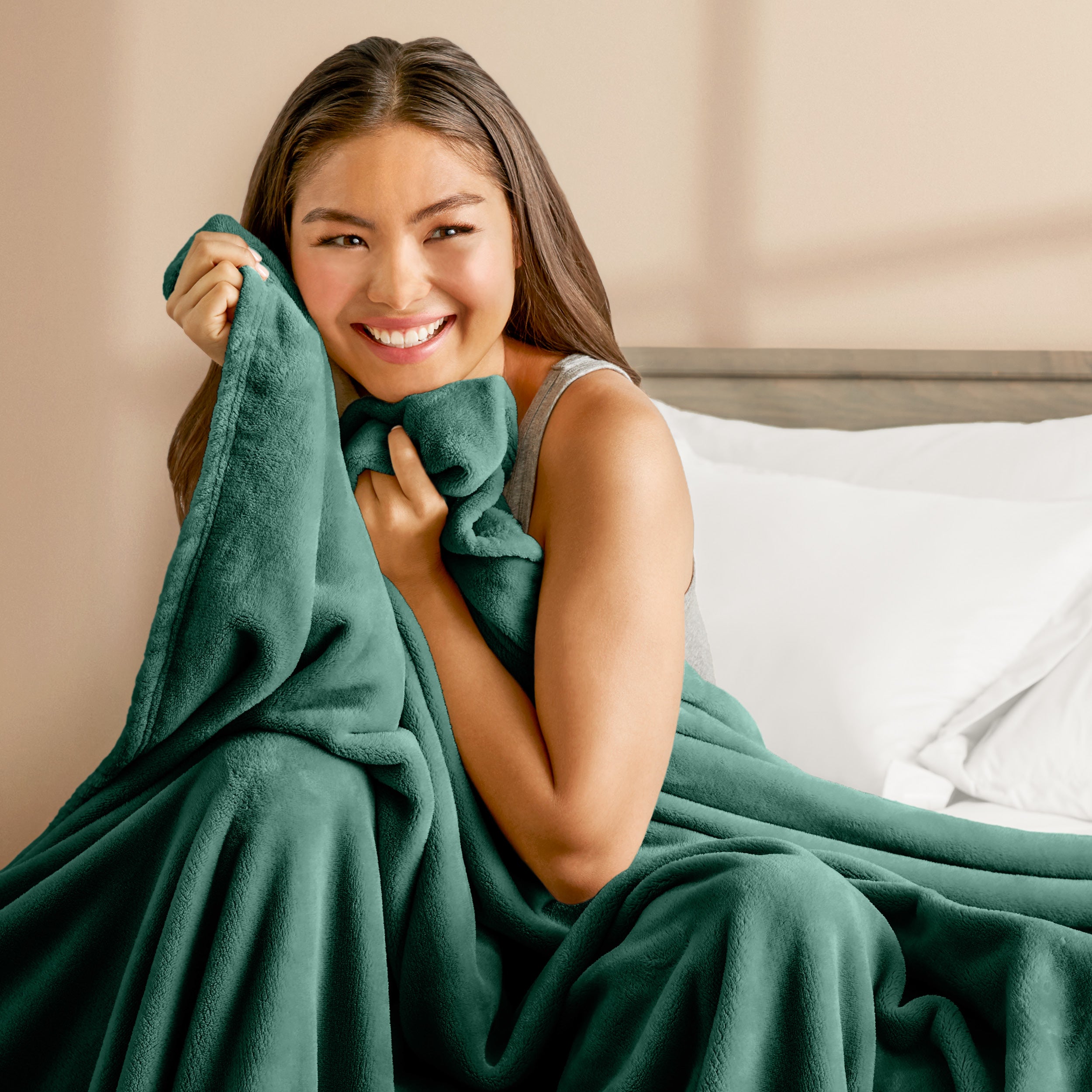 A woman sitting on a bed wrapped in a microplush blanket