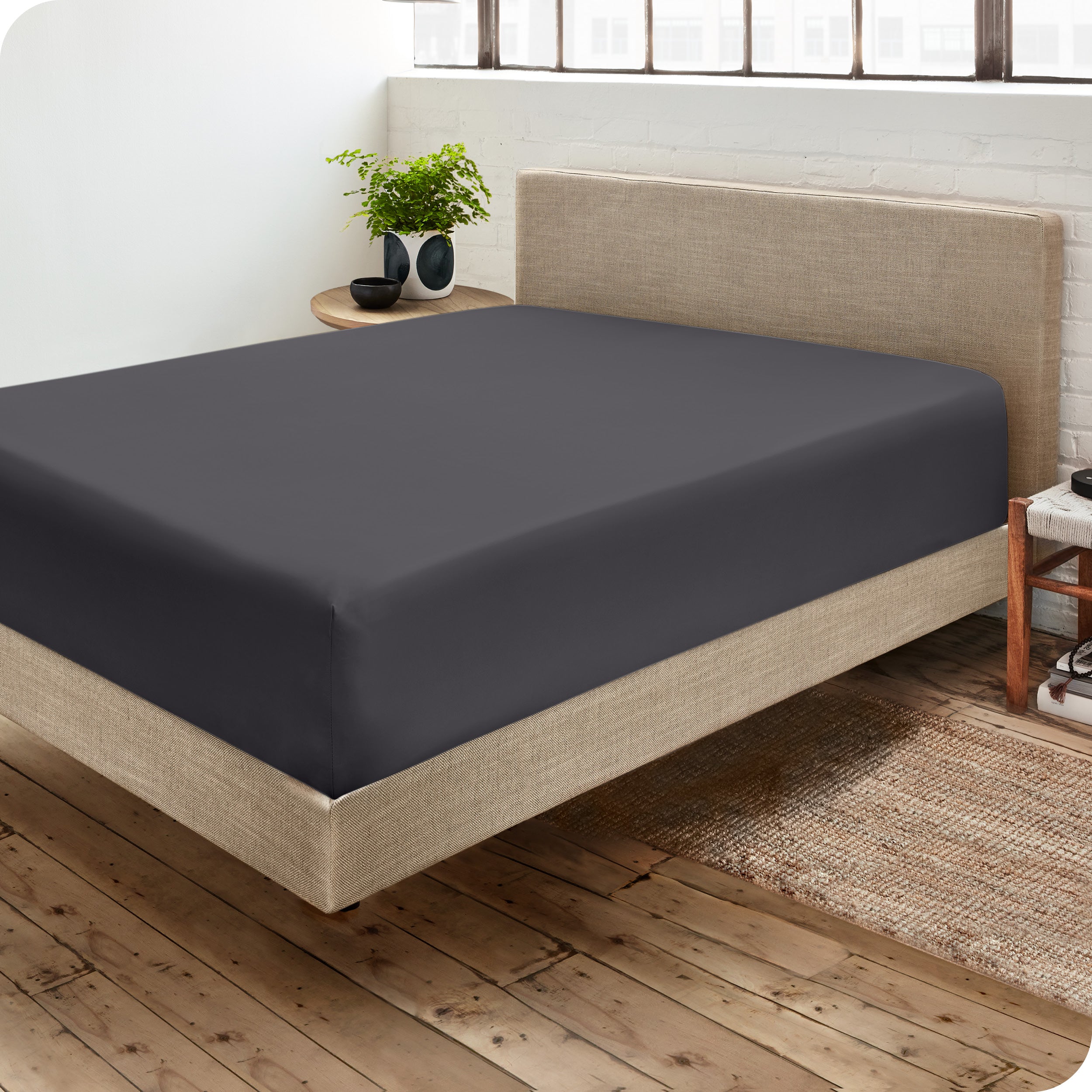 Corner view of a modern bed with a microfiber fitted sheet on the mattress. 