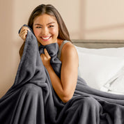 A woman sitting on a bed wrapped in a microplush blanket