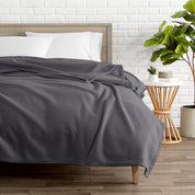 A polar fleece blanket on a bed next to a table and a large plant