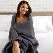 A woman sitting at the end of a bed with a fleece blanket wrapped around her shoulders